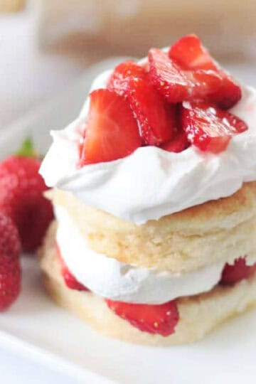 Biscuits, cream and strawberries stacked on white plate.