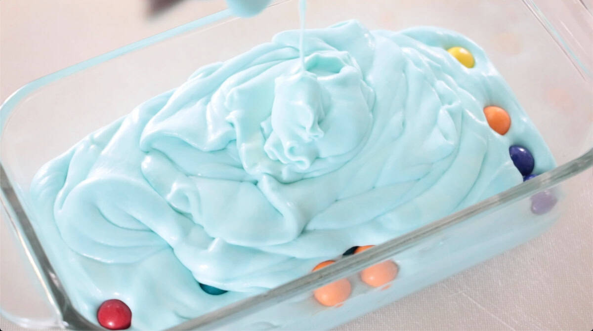 Ice cream mixture poured on top of gum balls in glass dish.