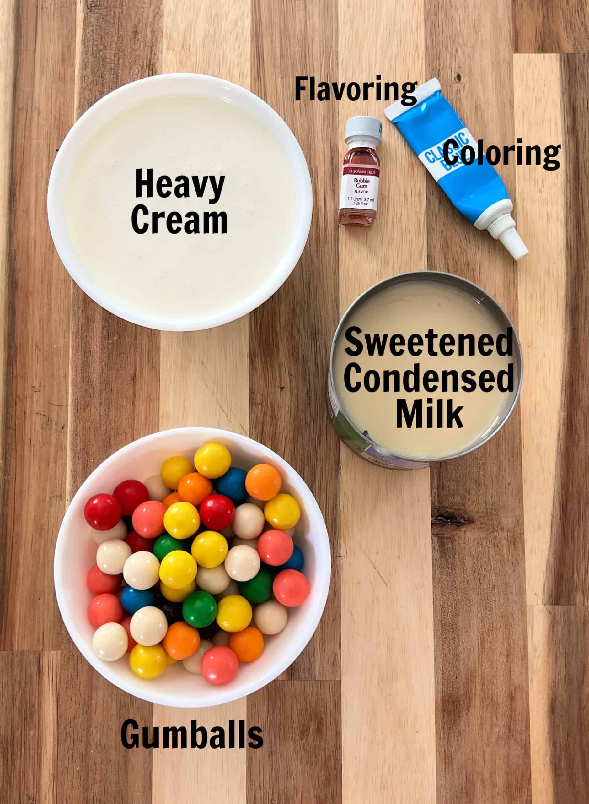 Bowls of heavy cream and gumballs with bottles of bubble gum flavoring and food coloring and a can of sweetened condensed milk.