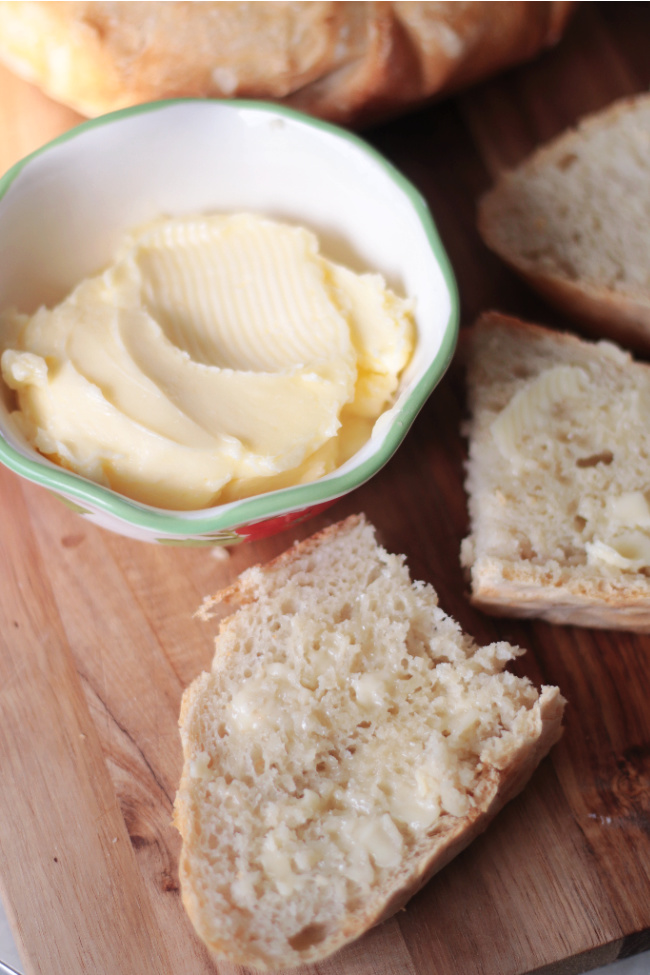 two slices of buttered bread next to bowl of homemade butter