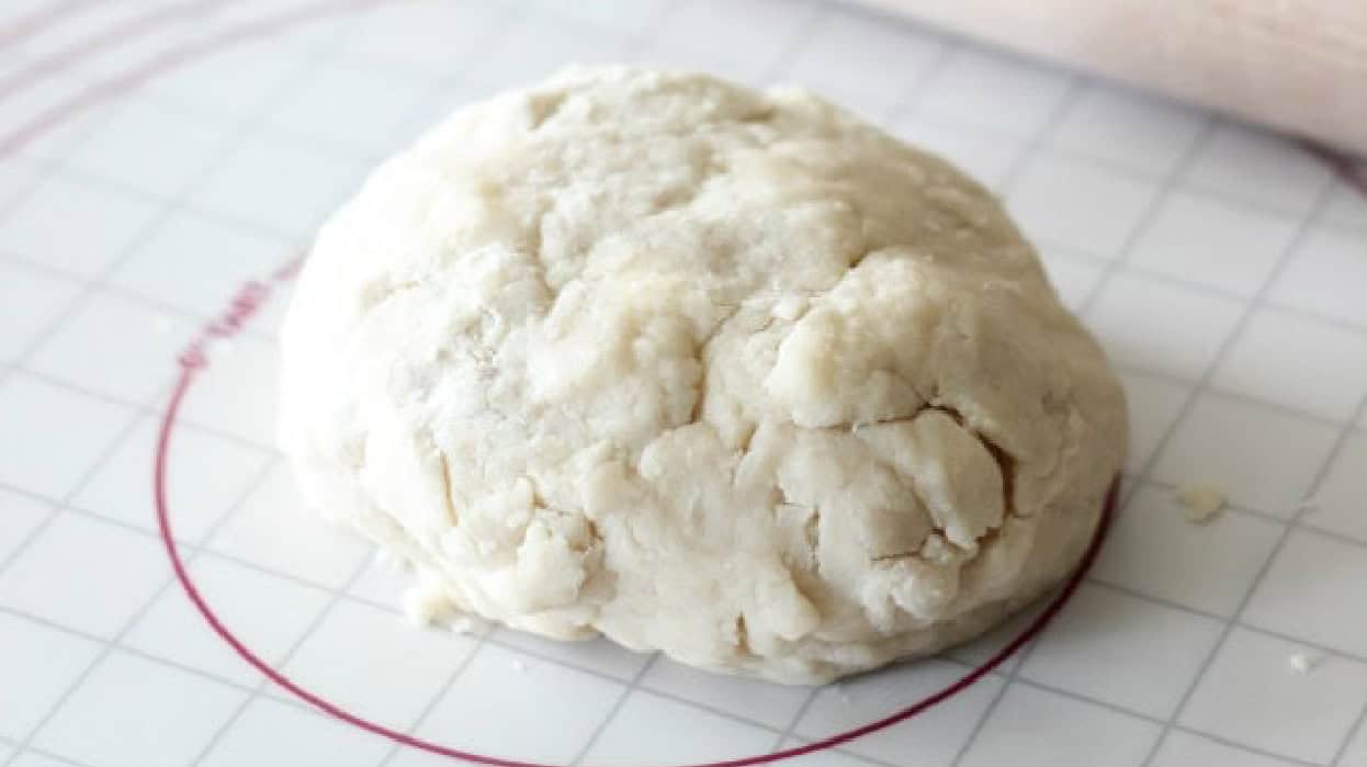 Ball of pie dough on rolling mat with rolling pin.