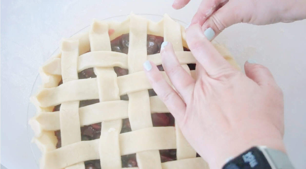 Hands crimping edge of cherry pie crust.