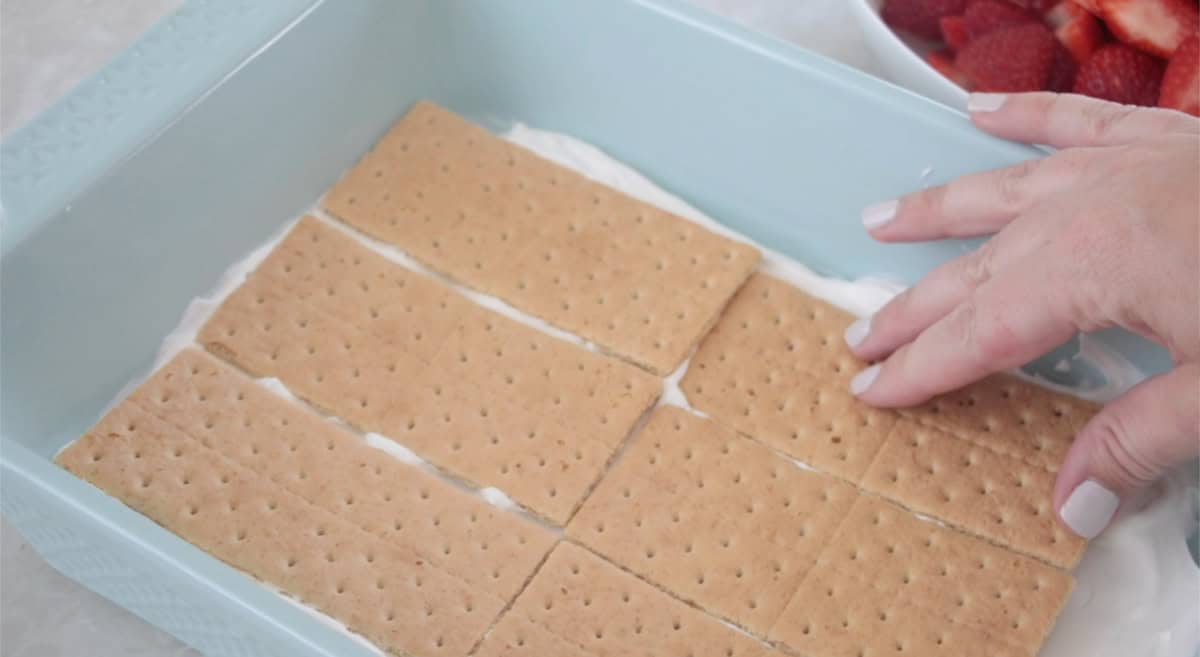 Blue baking dish with a layer of whipped cream and graham crackers.
