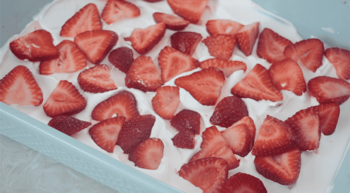 Blue baking dish with layer of whipped cream and strawberry slices.
