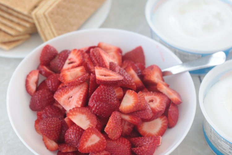 bowl of strawberries next to bowls of whipped cream and stacks of graham crackers