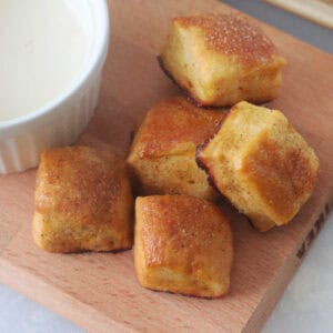Pretzel bites on wooden cutting board next to bowl of vanilla glaze.