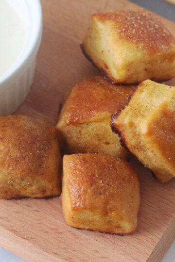 Pretzel bites on wooden cutting board next to bowl of vanilla glaze.