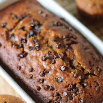 White loaf pan of pumpkin bread next to 3 muffins.