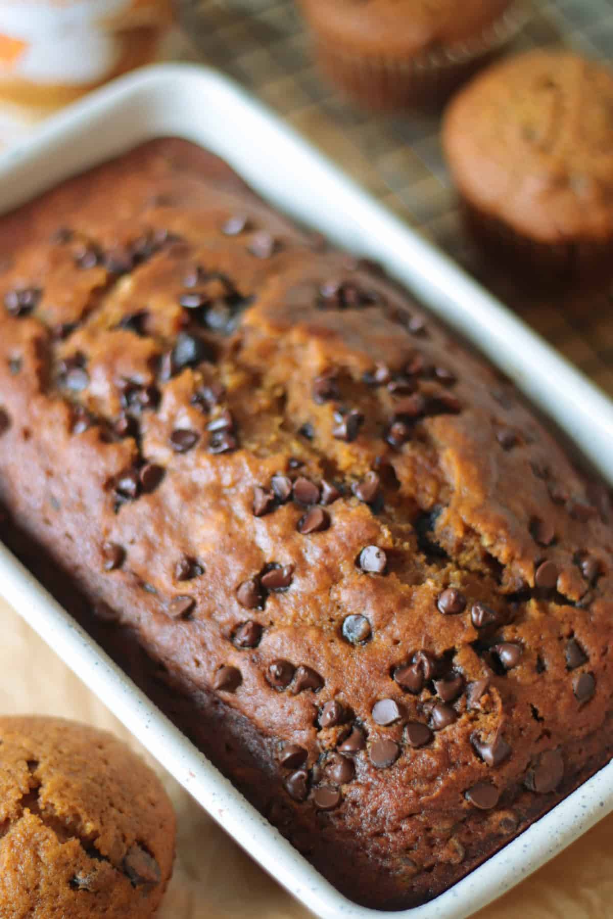 White loaf pan of pumpkin bread next to 3 muffins.
