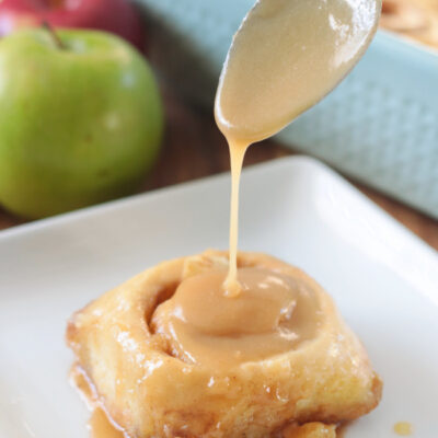 spoon drizzling caramel over cinnamon roll