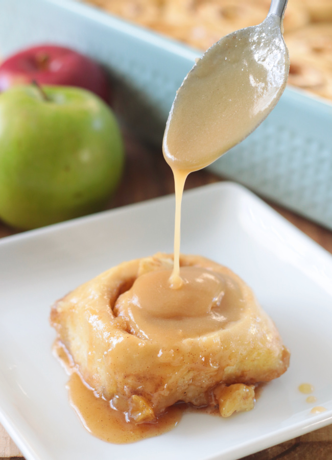 spoon drizzling caramel over cinnamon roll