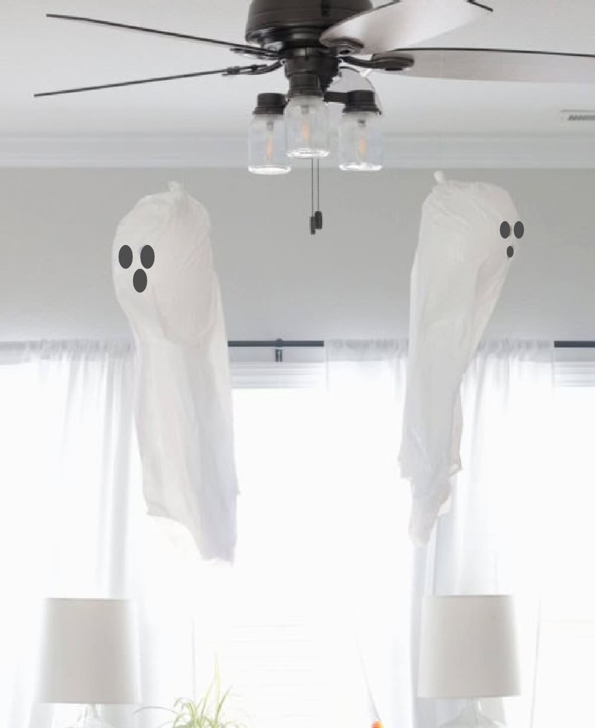 Two garbage bag ghosts hanging from ceiling fan.