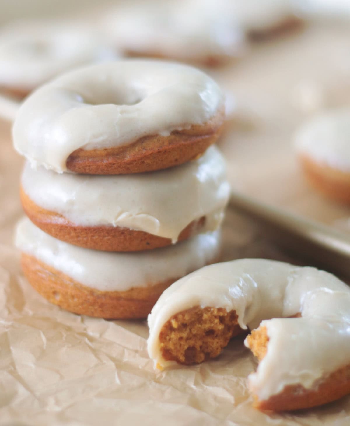 Stack of pumpkin donuts with glaze next to glazed donut on parchment paper.