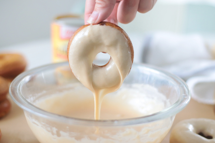 donut being dipped into maple glaze