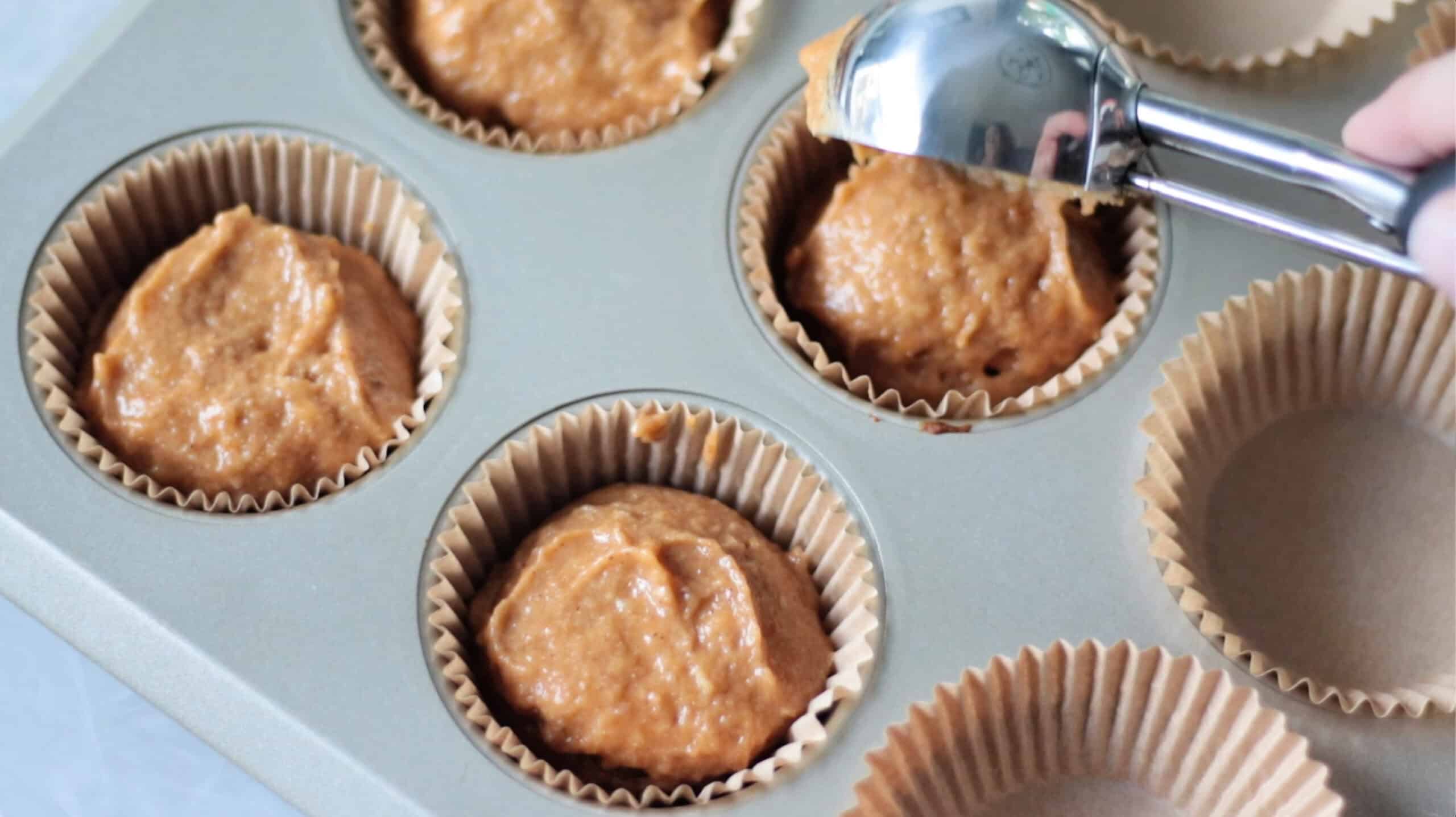 Metal muffin pan with pumpkin muffin batter scooped inside.