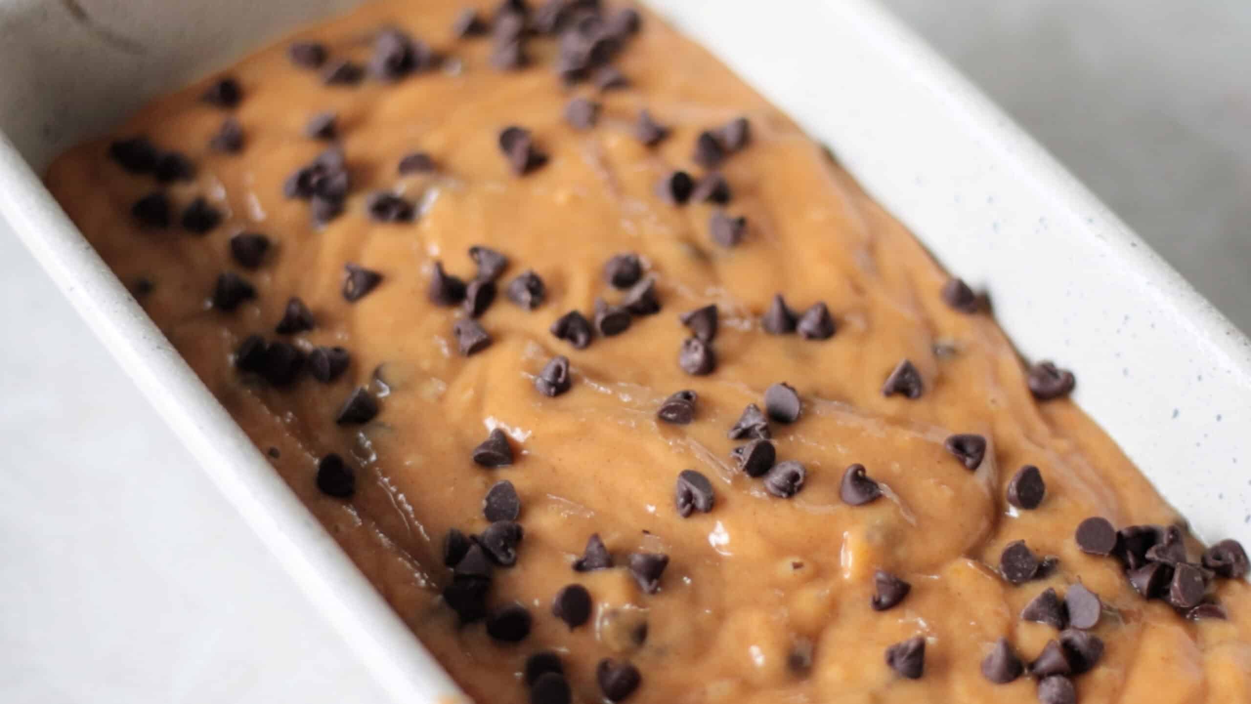 Pumpkin bread batter topped with chocolate chips in loaf pan.