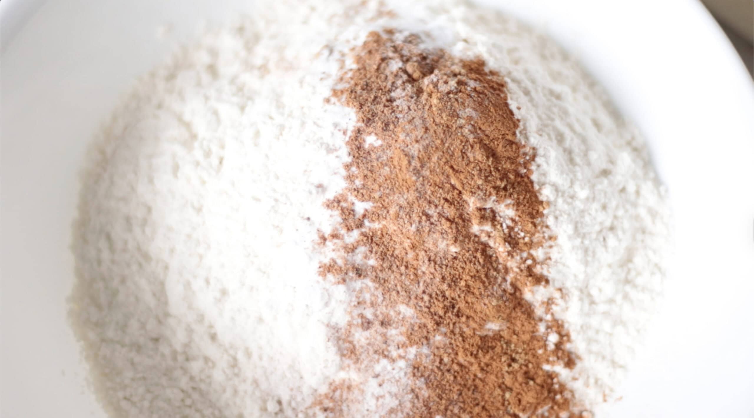 Dry ingredients for pumpkin bread in a white mixing bowl.
