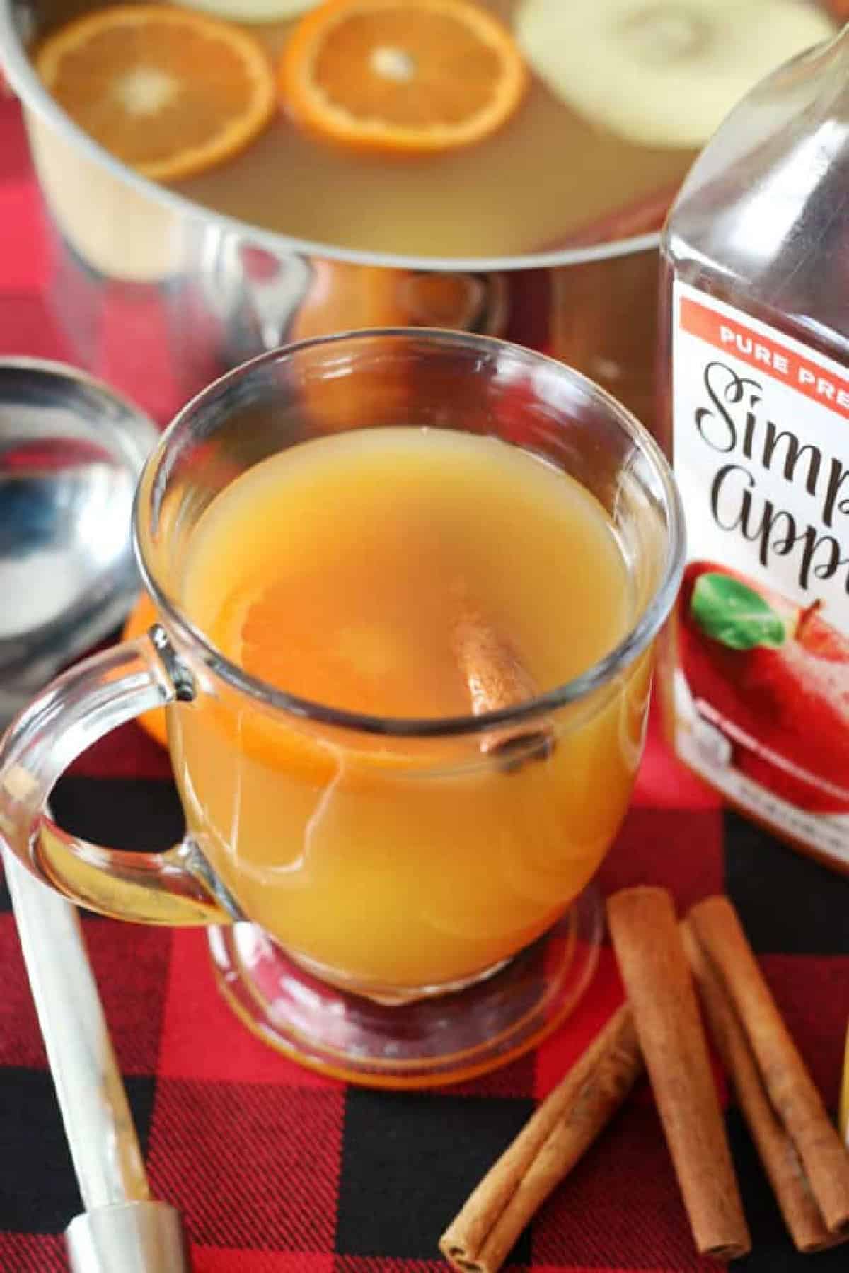 Clear mug of wassail with cinnamon sticks next to it.