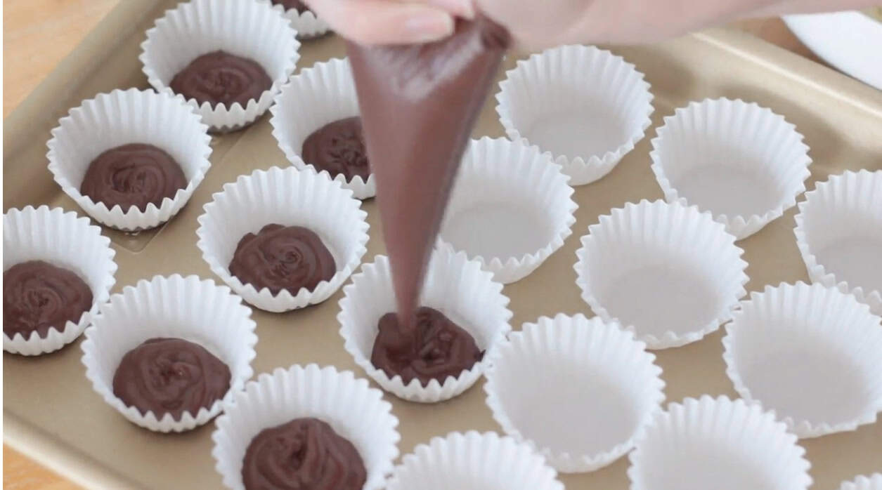 Mini cupcake liners being filled with chocolate.