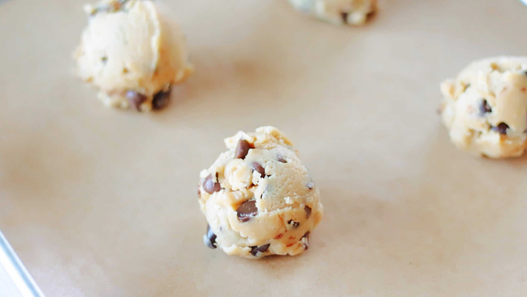 Scoops of cookie dough on baking sheet lined with parchment paper.