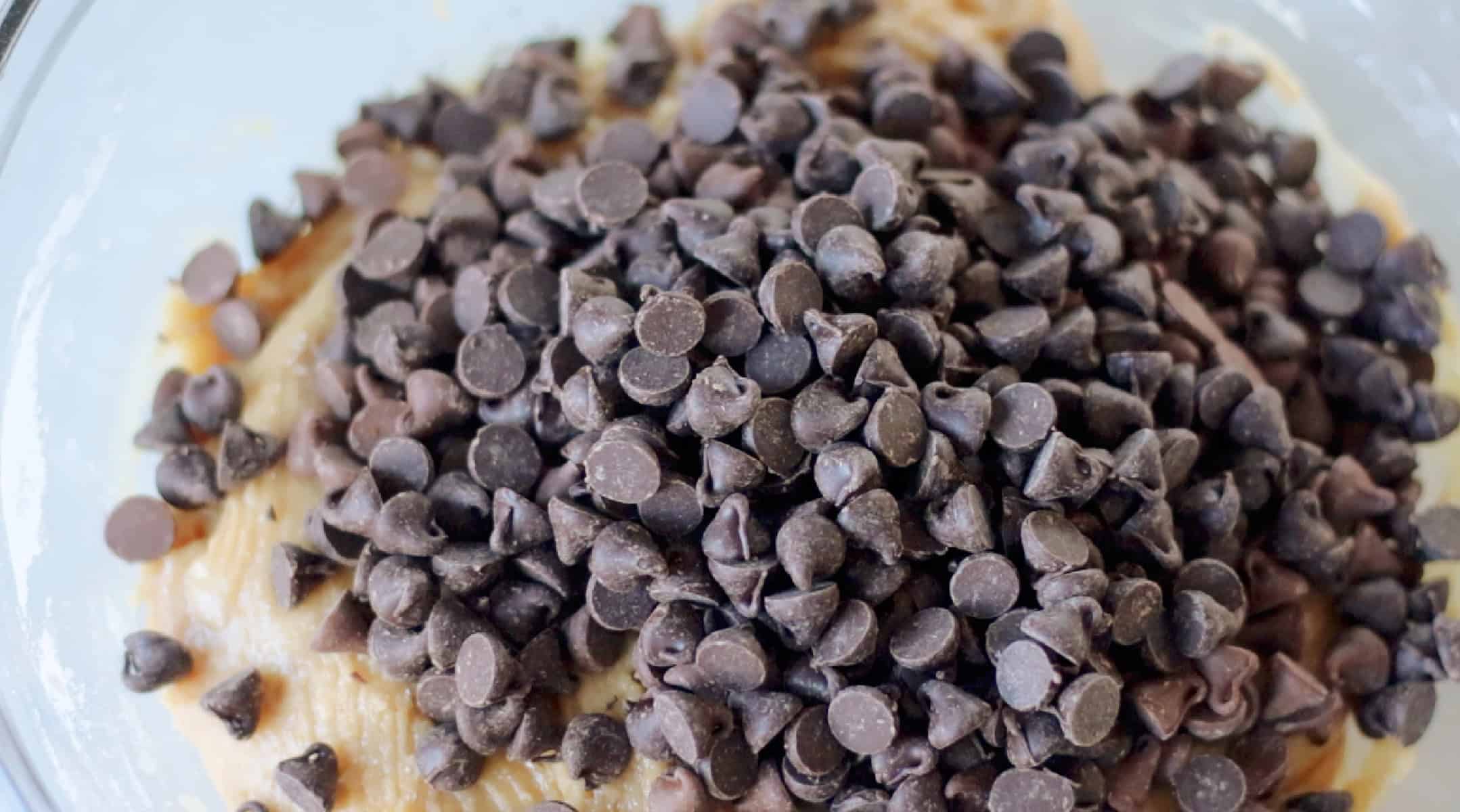 Chocolate chips poured into mixing bowl of cookie dough.