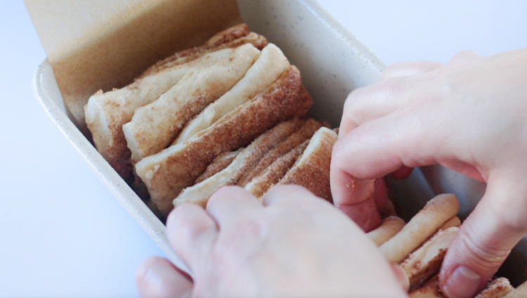 hands arranging bread dough slices in pan