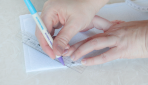 hand using a ruler to draw a line on fabric with fabric marker