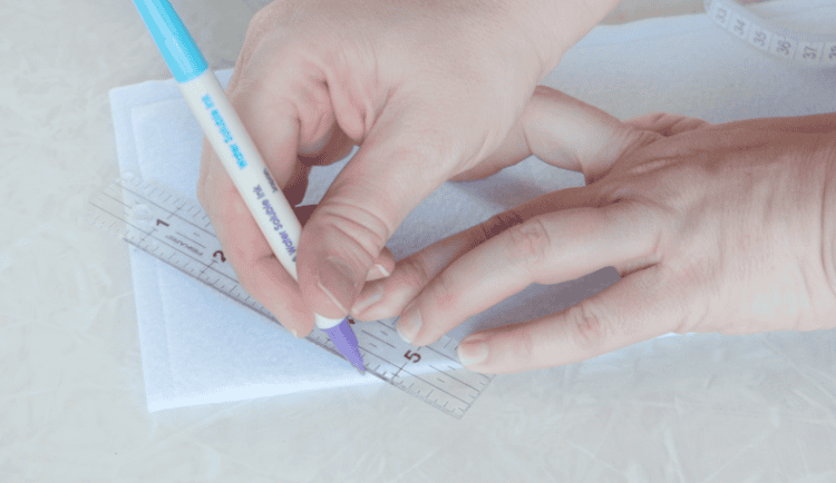 Hand using a ruler to draw a line on fabric with fabric marker.