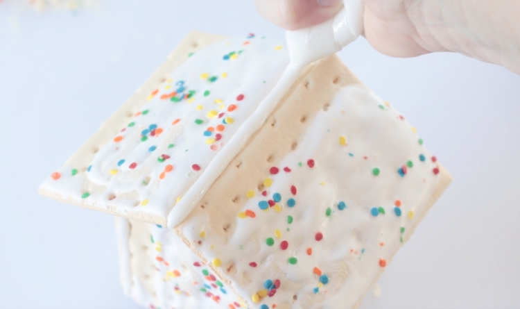 hand adding icing to roof of pop tart house in plastic baggie