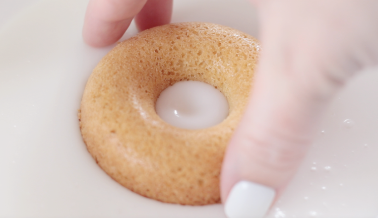 hand dipping donut into glaze