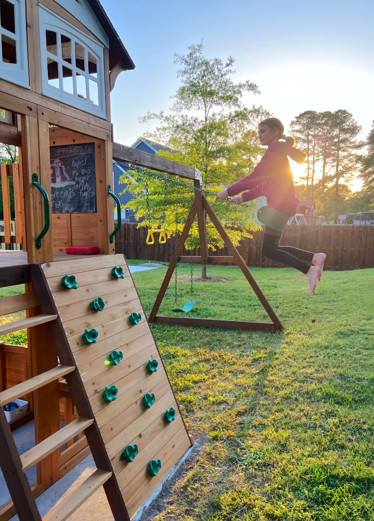 rock wall on swing set and child swinging on a swing