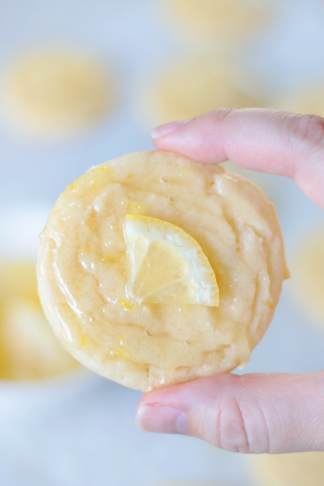 hand holding glazed lemon cookie with slice of lemon