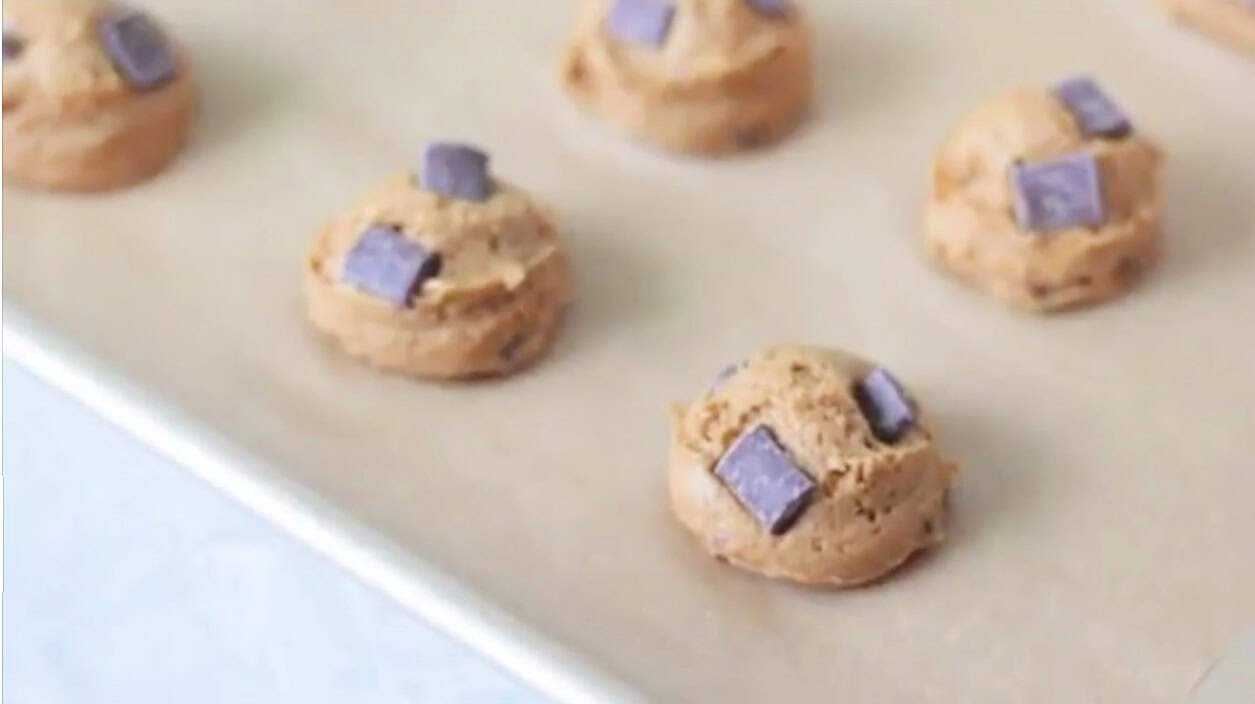 Cookie dough balls on parchment lined baking sheet.