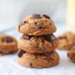 Stacked pumpkin cookies with chocolate chips on parchment paper.