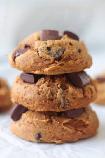 Stacked pumpkin cookies with chocolate chips on parchment paper.