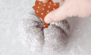hand gluing felt leave to the top of a sock pumpkin