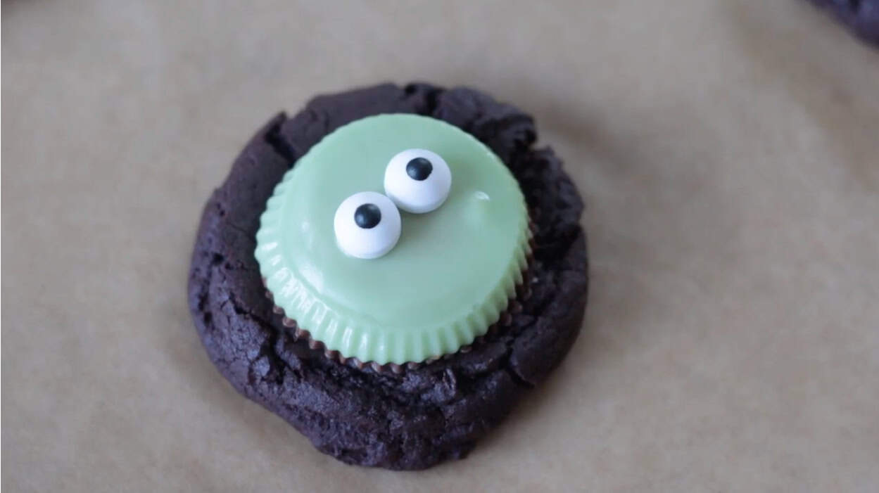 Candy eyes on top of green peanut butter cup cookie.