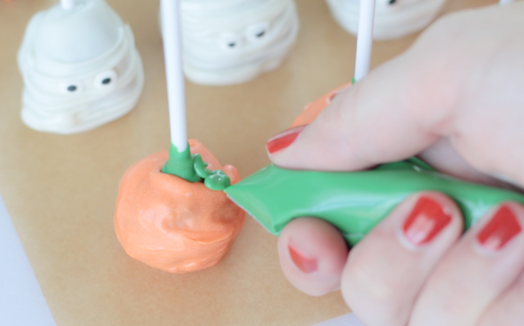 hand adding green candy melts to create pumpkin stem on lollipop