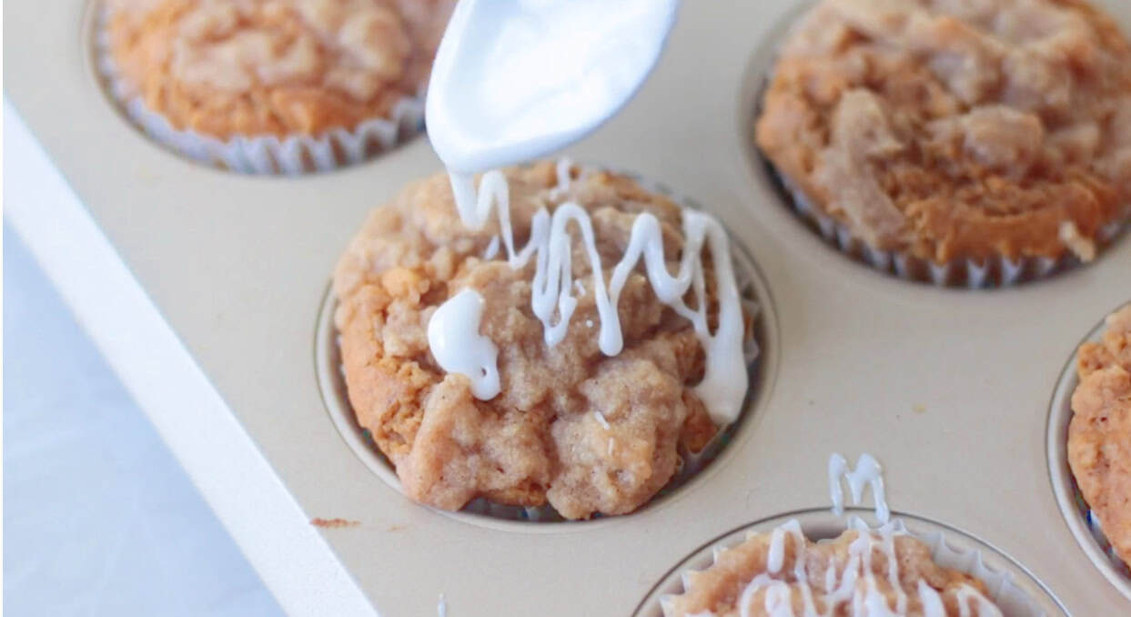 Spoon drizzling icing over baked pumpkin muffins.