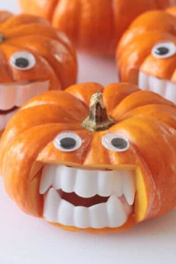 Four mini pumpkins with vampire fangs and craft eyes.