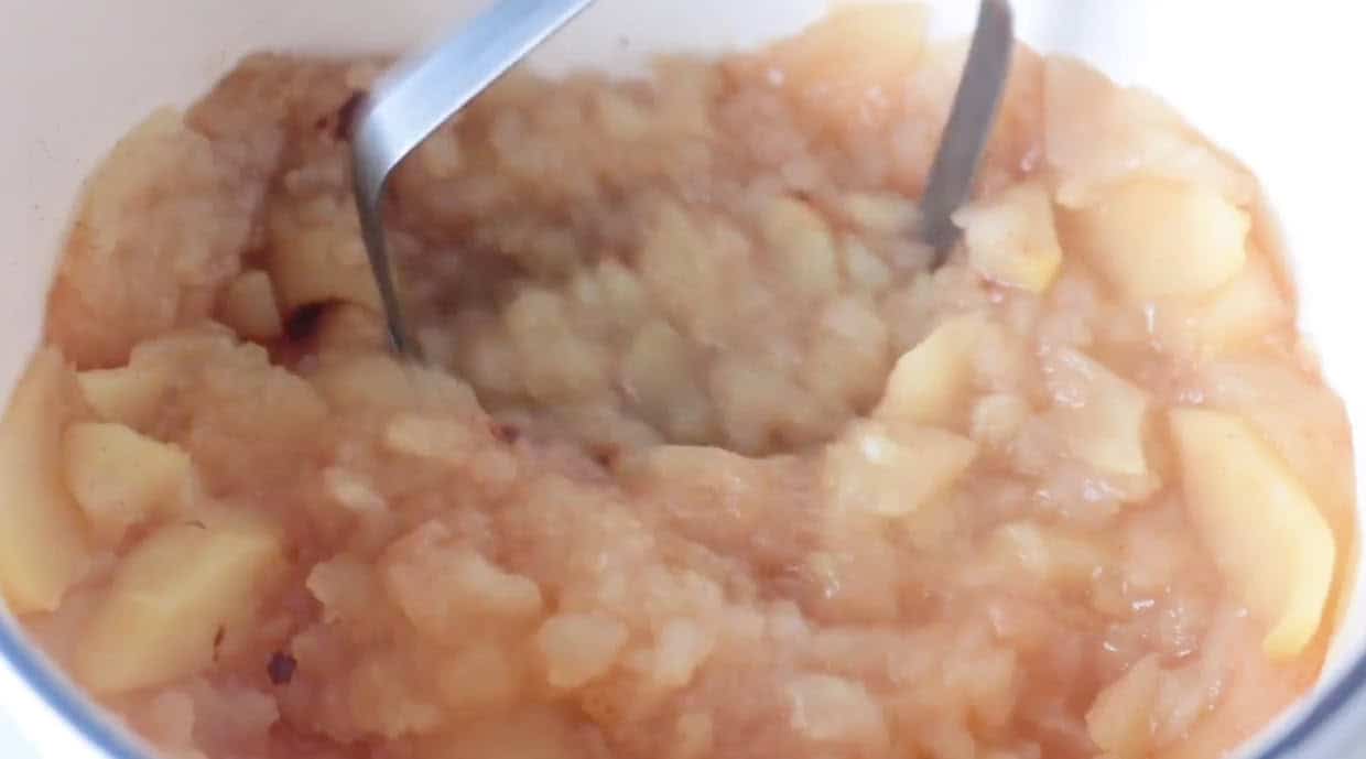 Potato masher mashing up baked apples in large pot.