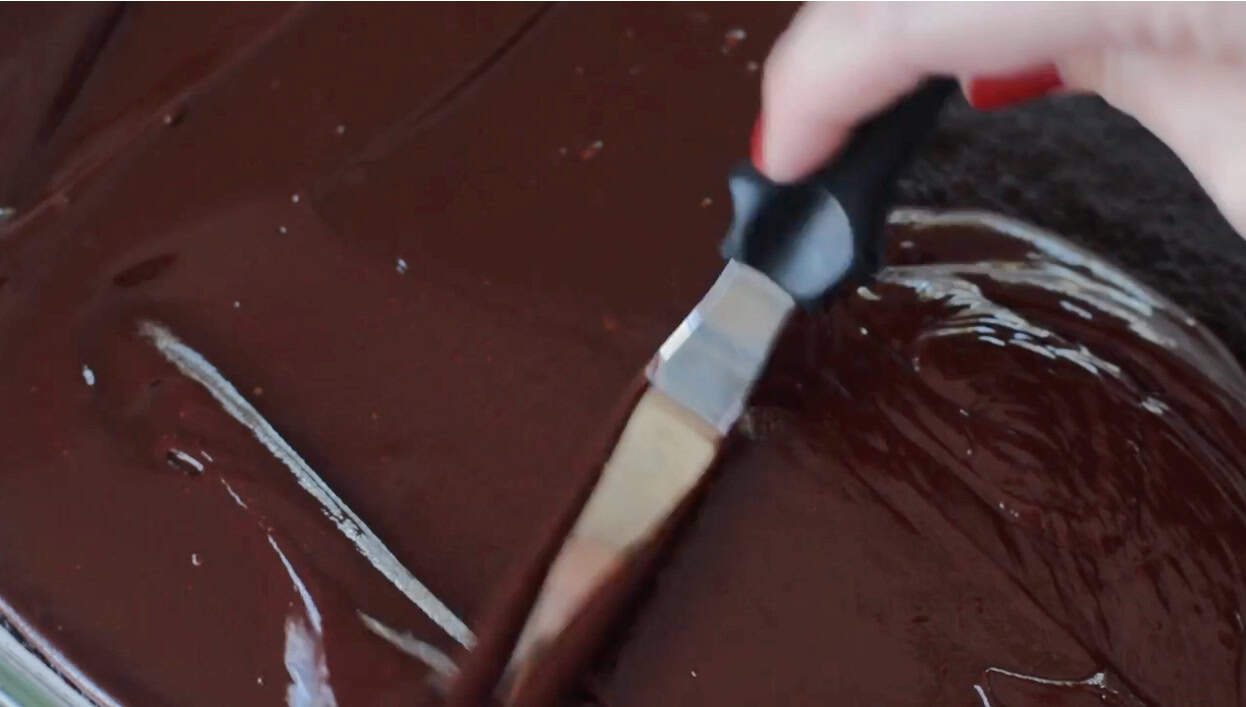 Spatula spreading ganache over brownies.