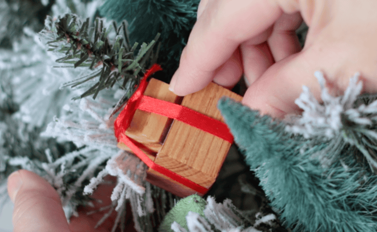 Hand placing wooden gift on wreath.