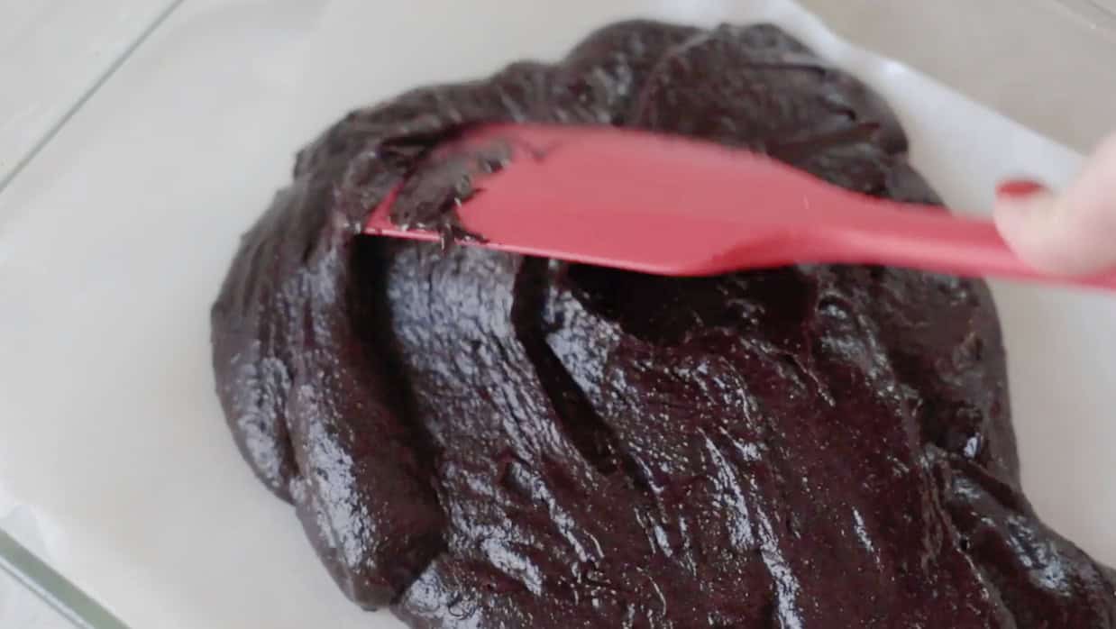 Rubber spatula spreading brownie batter in baking pan.