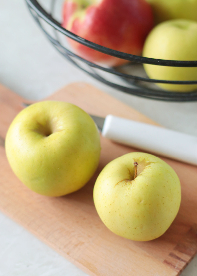 two apples and a knife on wood cutting board