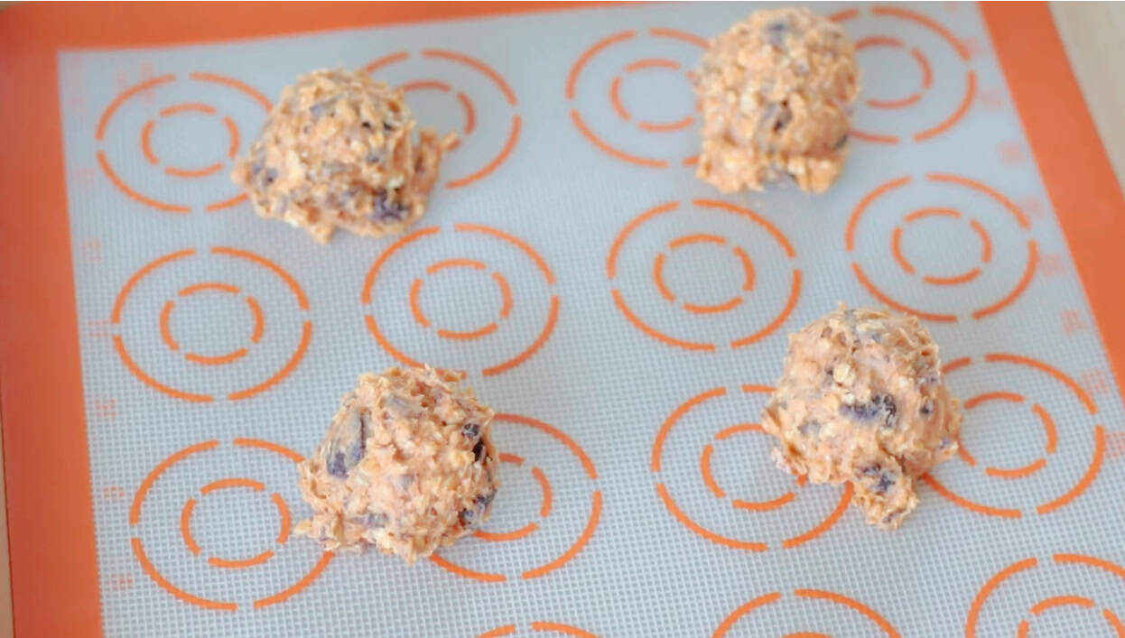 Scoops of pumpkin oatmeal chocolate chip cookie dough on silpat baking sheets.