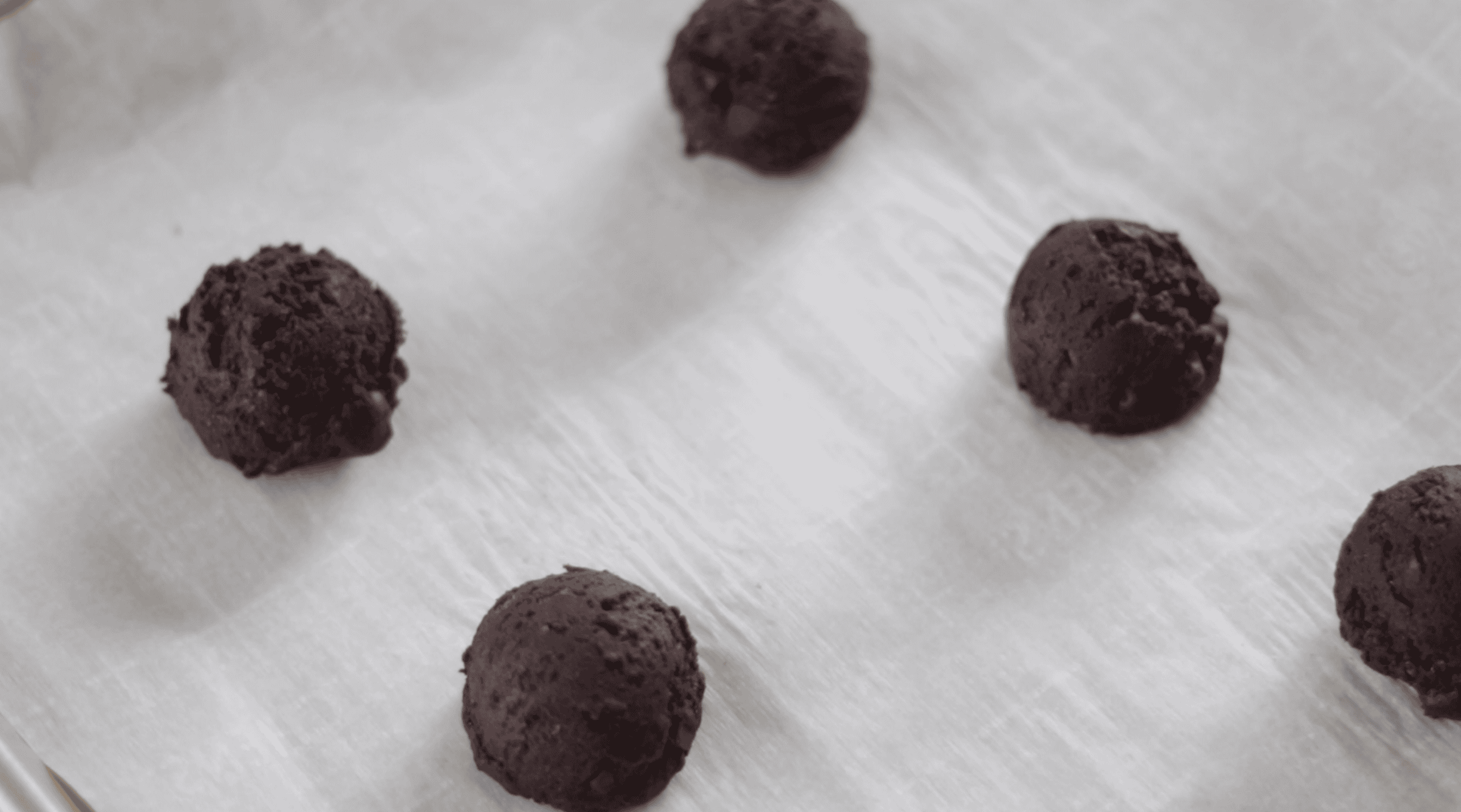 Balls of chocolate cookie dough on baking sheet.