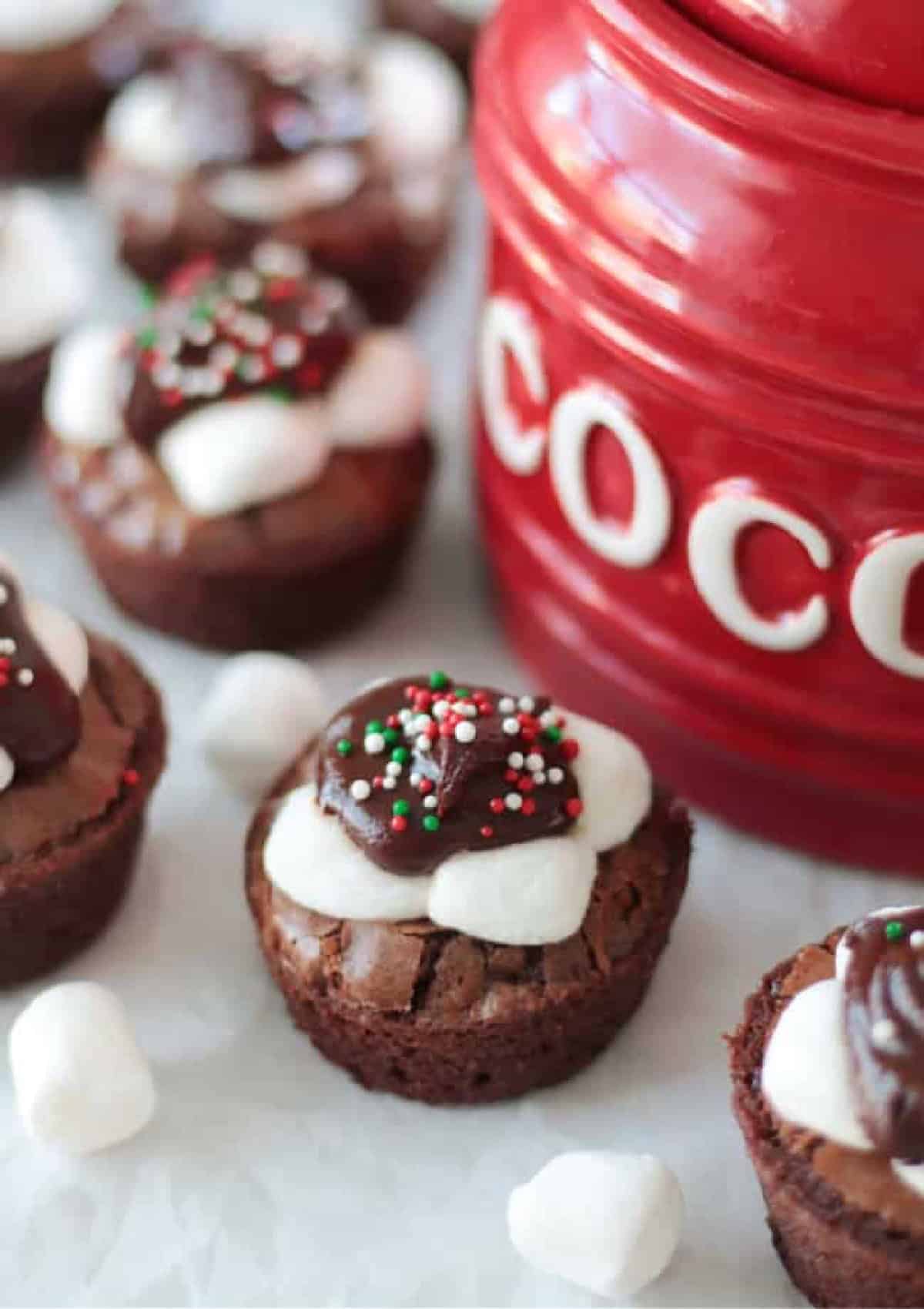 Hot cocoa brownies next to red ceramic jar of cocoa.