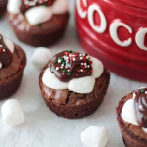 Brownie bites with chocolate and marshmallows next to red cocoa jar.
