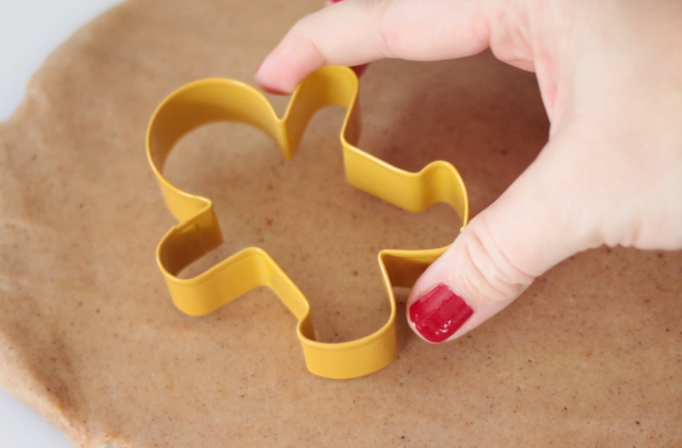 hand pressing gingerbread cookie cutter onto play dough